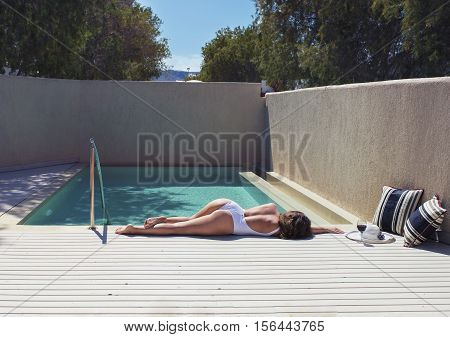 female in a swimsuit lying near the pool with hat and wine