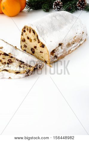 Sliced Christstollen on white background with fresh oranges fir and pine cones in the background. In the foreground lots of copy space.