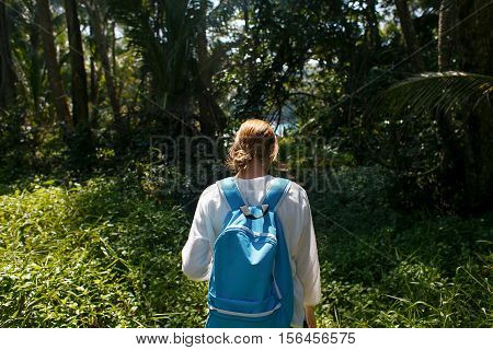 Back view of young woman with backpack outdoors discovering jungle