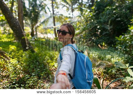 Follow me. Travel concept. Back view of young woman with backpack outdoors discovering jungle holding boyfriend's hand.