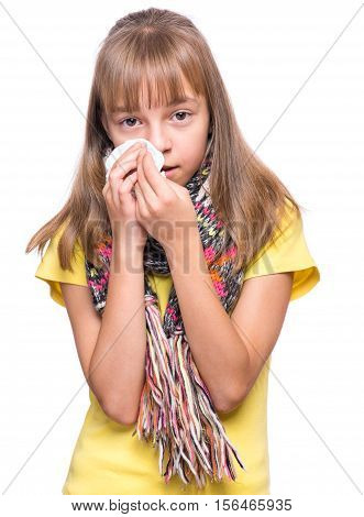 Healthcare and medicine concept - ill little girl with flu blowing nose. Kid wipes a nose a napkin. Child wearing yellow t-shirt and scarf.