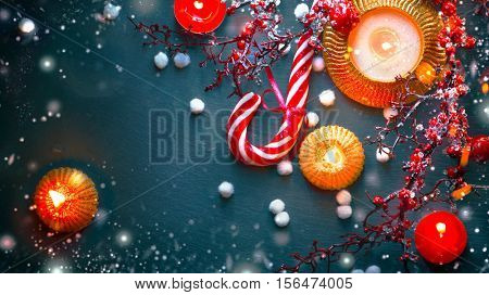 Christmas Holiday Background with Candy Cane, decorations, candles, garland and evergreens border over dark background table. Christmas and New year food. Christmas dinner, served table, decorations