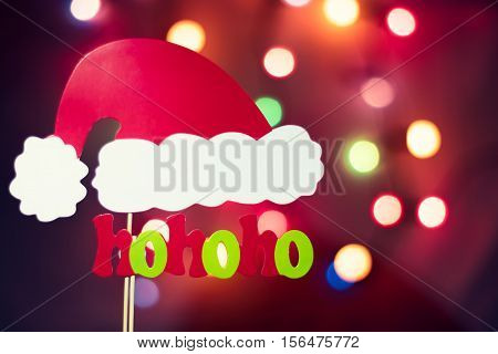 Christmas Santa Claus "hohoho" exclamation with colorful tree lights bokeh background with a hat made of photo booth props. Copy space at the top right corner.