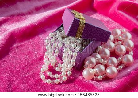A purple box with pink pearl strings on a crimson velvet