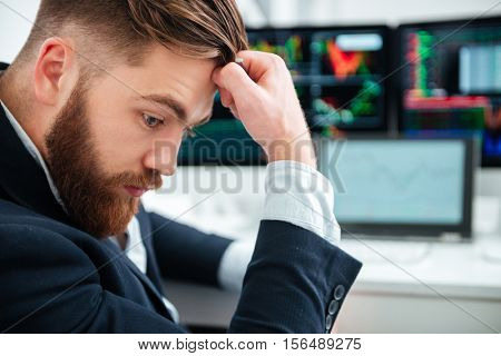 Profile of pensive bearded young businessman sitting and thinking in office