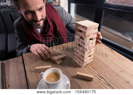 Board games. Joyful nice amused man playing jenga and having fun while relaxing after work