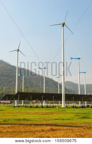 solar panels with wind turbines against mountanis landscape against blue sky