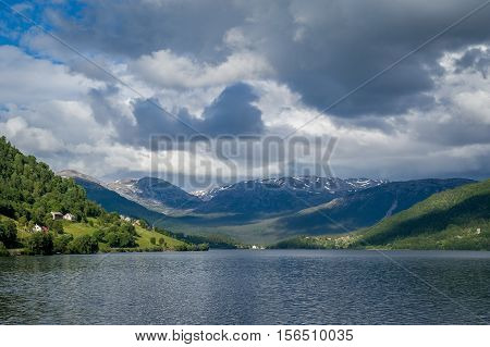 Panoramic view of Norway fjord with dramatic clouds and villages under the mountains. Scandinavian landscapes.