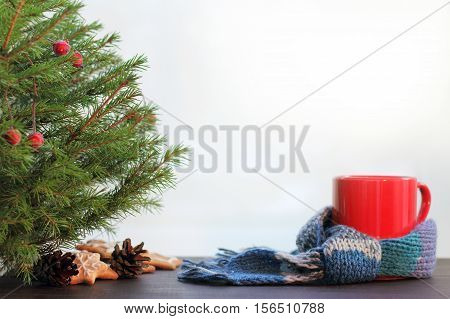 mug wrapped in red scarf near a festive fir tree with decorations and gingerbread / warming Christmas atmosphere