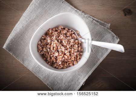 Boiled buckwheat with spoon in ceramic bowl.