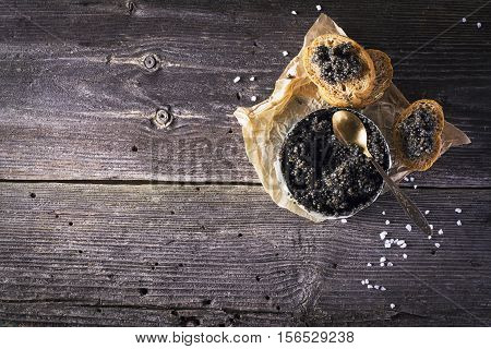 Black Astrakhan Russian salted sturgeon caviar in a can on a dark background with a wooden spoon and slices of bread. Snacks and luxury holidays. selective focus