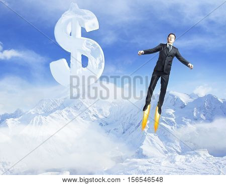 Young superman flying in bright blue sky with creative dollar sign above snowy mountains. Success concept