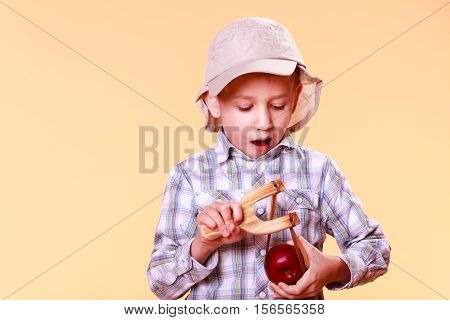 Nature and free time prankster little boy. Child have fun with wooden sling shot and fruit hold apple.