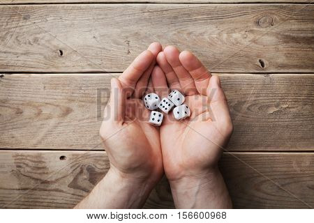 Man holding in hand white dice over the wooden table top view. Gambling devices. Game of chance concept.