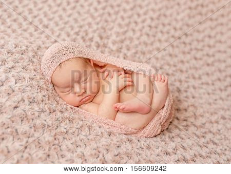 lovely newborn curled up asleep, wrapped in pink diaper on knitted blanket