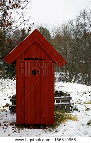 Red outhouse toilet in wintertime. Front view.