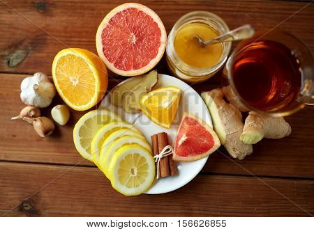 health, traditional medicine, folk remedy and ethnoscience concept - cup of ginger tea with honey, citrus and garlic on wooden background