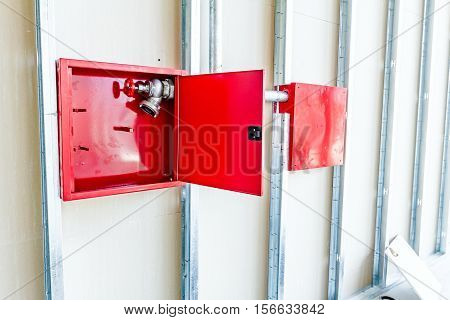 Red fire hydrant cabinet with extinguish valve is placed in an unfinished dry wall.