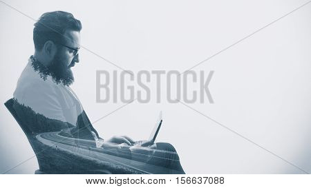 Concept depicting business trip. Image created using multiple exposures. Black and white portrait of a bearded businessman with a laptop and a long road. There is space for your text.