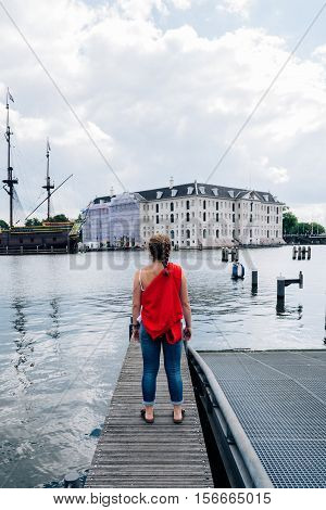 Amsterdam Netherlands - August 1 2016: Woman on jetty looking at The National Maritime Museum and old ship in Amsterdam a cloudy day