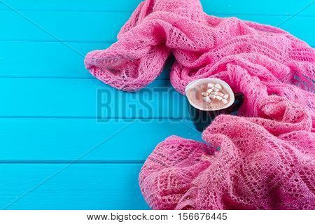 Cozy winter home background cup of hot cocoa with marshmallow old vintage books and warm knitted sweater on white painted wooden board background.
