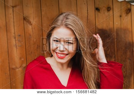 Happy blonde girl with red clothes and lips on a wooden background