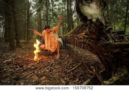 Caveman in animal skin kindles a fire in the forest