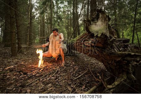Caveman in animal skin kindles a fire in the forest