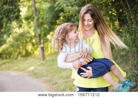 Beautiful mother spinning her cute little son. Sunny summer day in nature.