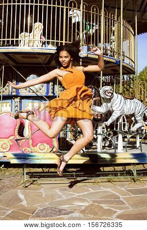 cool real modern teenage girl with candy near carousels at amusement park walking, having fun