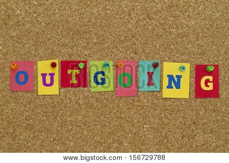 Outgoing word written on colorful sticky notes pinned on cork board.