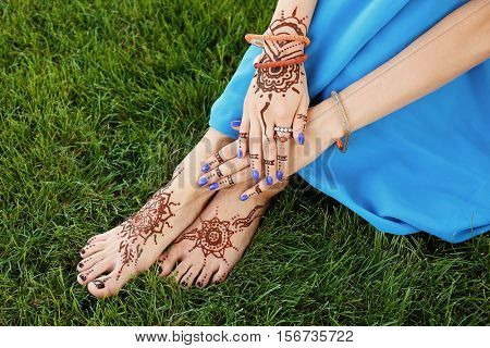 Female legs and hands with henna tattoo on green grass background