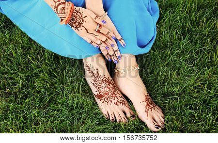Female legs and hands with henna tattoo on green grass background