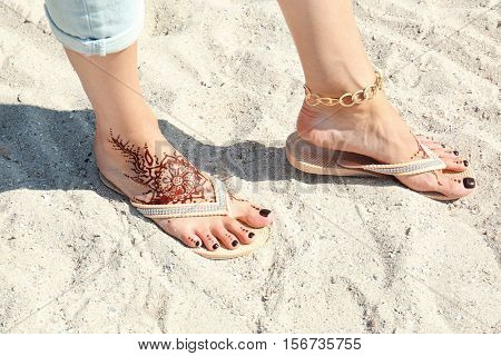 Female legs with henna tattoo on beach sand background