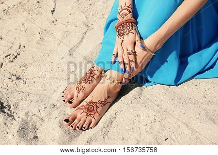 Female legs and hands with henna tattoo on beach sand background