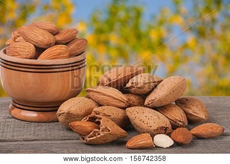 almonds in a bowl on the old wooden board with blurred garden background.