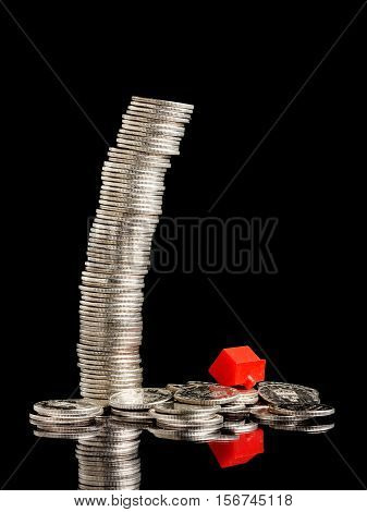 A tall stack of coins has failed togather with a red small plastic house.