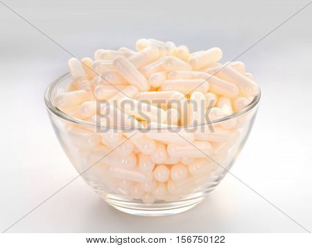 Beige toned capsules pile in a glass bowl. Medication drug addiction and nutritional supplements concept