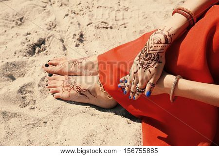 Female legs and hands with henna tattoo on beach sand background