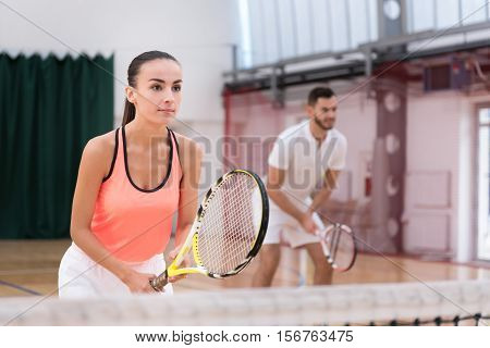 Serious set. Pleasant beautiufl concentrated woman holding racket and playing tennis while her male sportsman standing in the background
