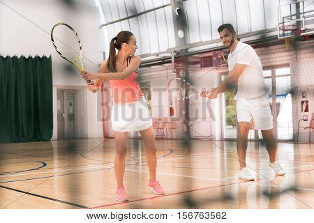 Train with pleasure. Positive delighted woman holding racker and learning how to play tennis while professional trainer teaching her