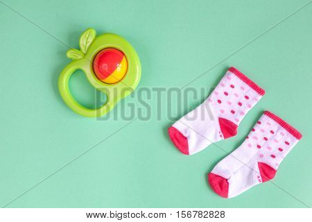 baby rattle and socks on green background top view