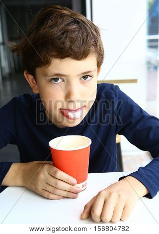 preteen boy with cappuccino coffee in paper glass show scum foam on tongue close up portrait in fast food restaurant cafe