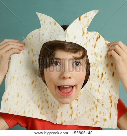 preteen handsome boy make fun cut hole in pita thin bread and look through the hole laughing smiling close up photo jester buffoon representation