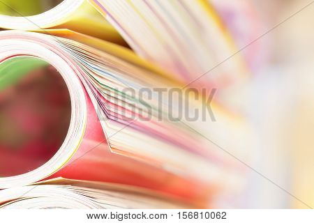 Close up edge of colorful magazine stacking roll with blurry bookshelf background for publication and publishing concept extremely shallow DOF