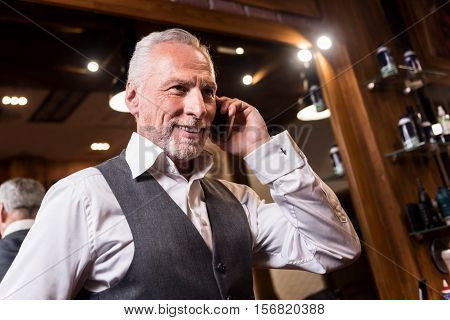 Discussing important bargain. Low angle of nice smiling senior businessman standing and talking on mobile phone.