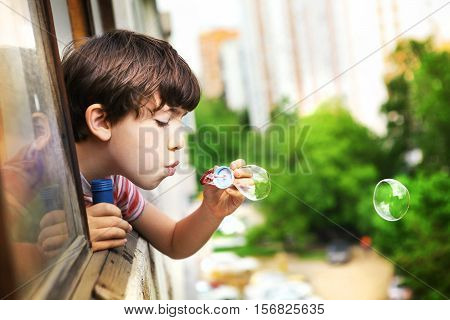 preteen handsome boy with soap bubbles lood out of the window