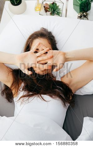 Beautiful young Caucasian smiling woman covering her eyes on bed