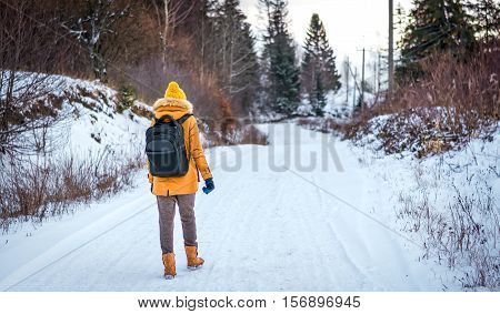 girl in a yellow jacket with a backpack walking in Ukrainian Carpathians in the winter woods
