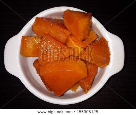 Slices of pumpkin with sugar baked in the oven. The white plate on a black background